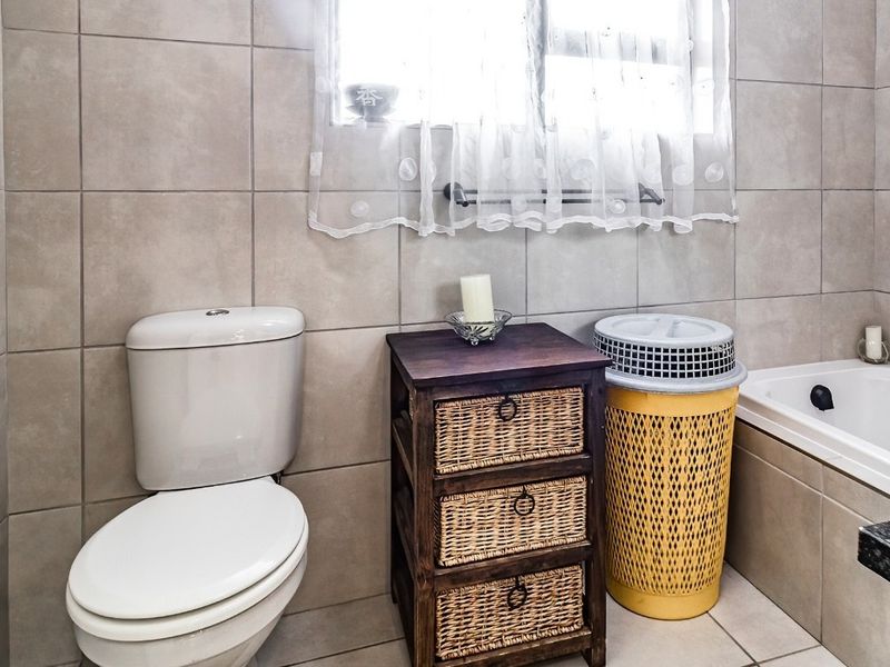 A functional bathroom featuring neutral wall and floor tiles, a standard toilet, and a built-in bathtub with a window for natural light.