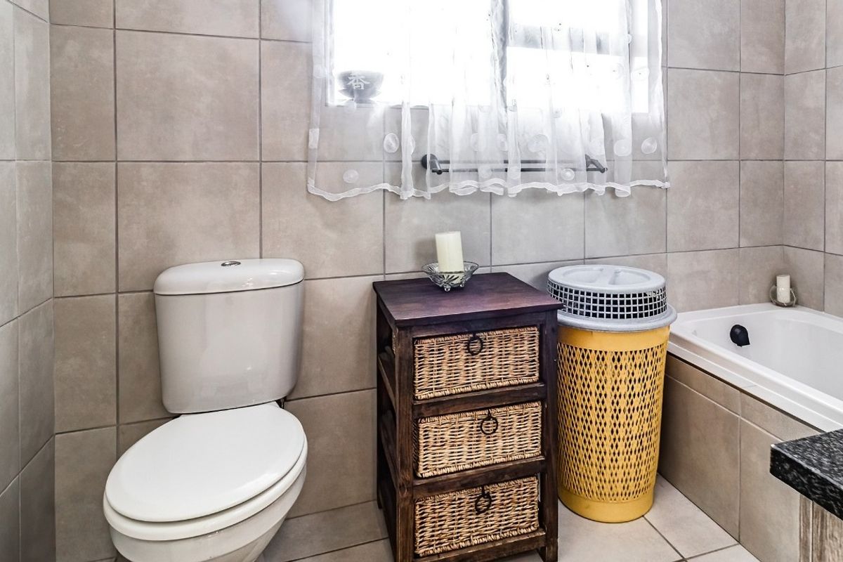 A functional bathroom featuring neutral wall and floor tiles, a standard toilet, and a built-in bathtub with a window for natural light.