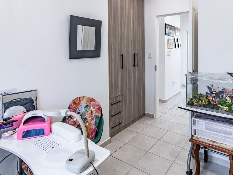 A bedroom featuring neutral tiled flooring and modern wood-grain built-in cupboards, currently utilized as a workspace.