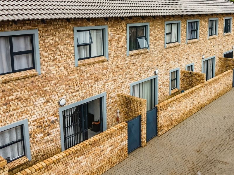 An elevated view of a multi-unit townhouse complex featuring face brick facades, tiled roofing, and private paved courtyard entrances with security gates.