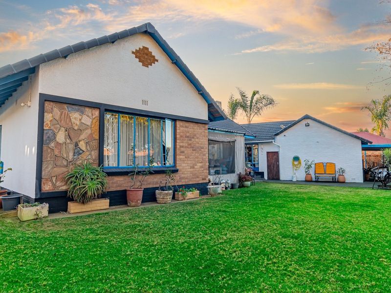 Rear view of the house featuring a well-maintained lawn, stone-clad exterior wall, and a paved patio area under a tiled roof.