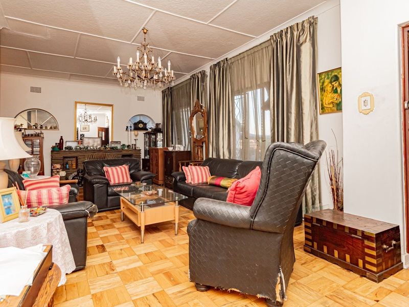 A spacious living room featuring classic parquet flooring, a decorative crystal chandelier, and traditional ceiling tiles, offering a solid foundation for modern updates.