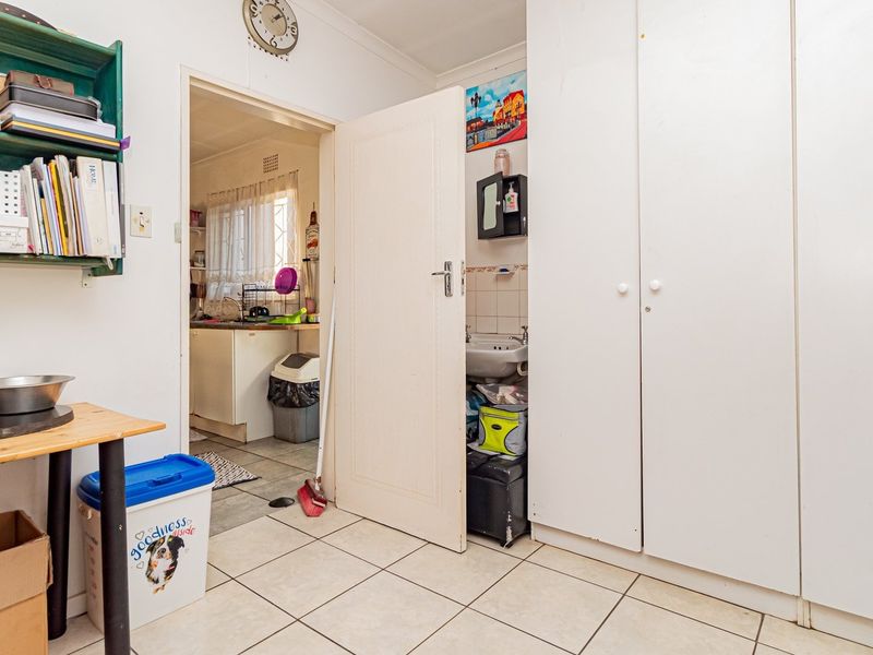 A functional laundry area featuring tiled flooring, built-in storage cupboards, and a small sink, with direct access to the kitchen.