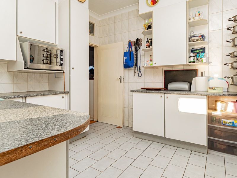 A functional kitchen featuring white cabinetry, tiled backsplash, and tiled flooring, offering a dated aesthetic with potential for modern renovation.