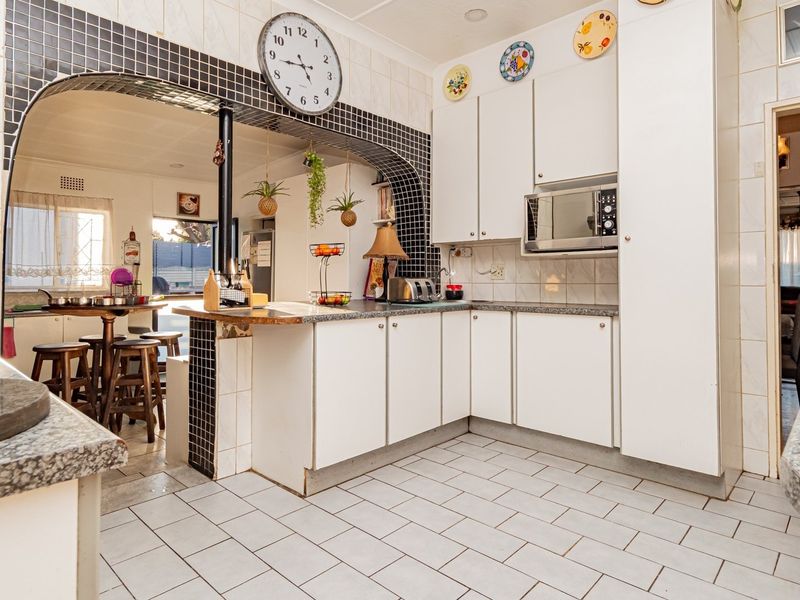 A functional kitchen featuring white built-in cabinetry, tiled backsplash, and a breakfast bar opening into an adjacent dining area.