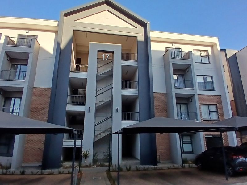 Front elevation of a modern multi-story apartment complex featuring brick and render facade, external stairwell, and covered parking bays.