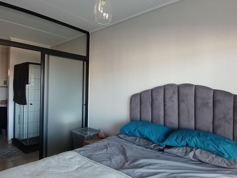 A modern bedroom featuring a sleek black-framed glass partition wall that separates the sleeping area from an en-suite shower room.