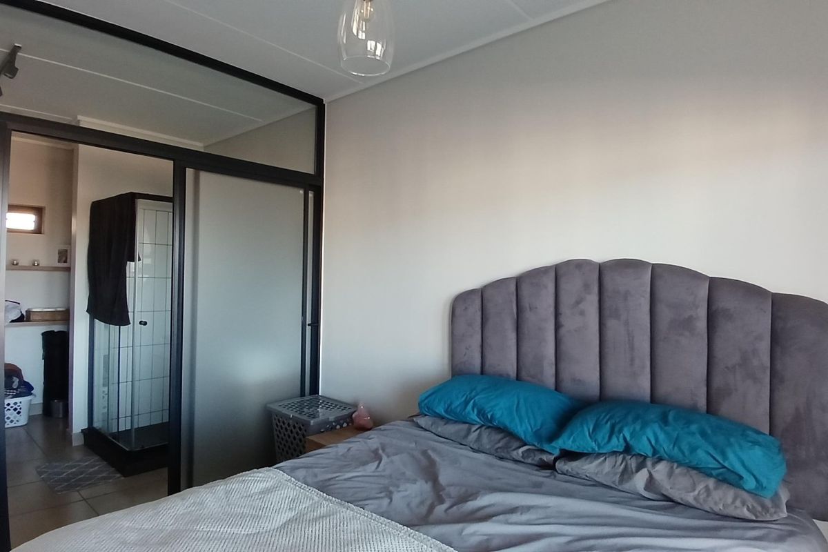 A modern bedroom featuring a sleek black-framed glass partition wall that separates the sleeping area from an en-suite shower room.