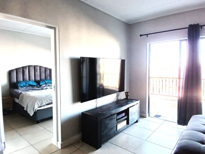 A bright living room featuring tiled flooring and a sliding glass door providing direct access to an outdoor balcony.