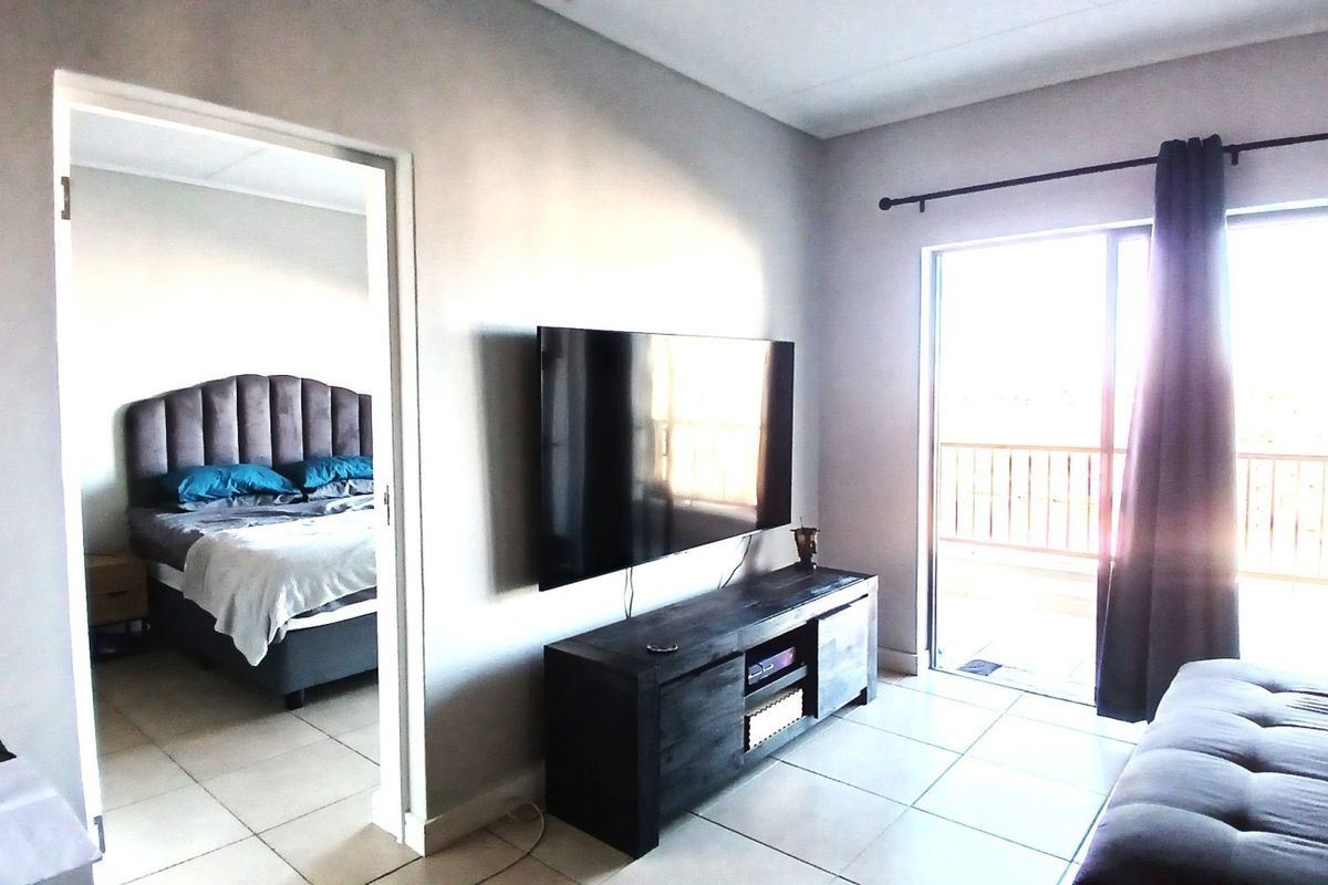 A bright living room featuring tiled flooring and a sliding glass door providing direct access to an outdoor balcony.