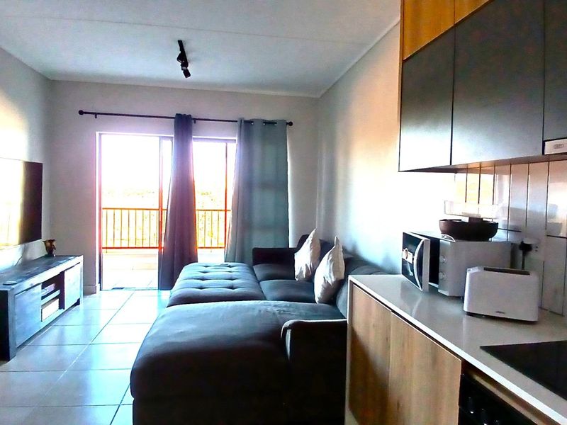 Open-plan living area featuring a modern kitchen with built-in cabinetry and tiled flooring, leading directly to a balcony through sliding glass doors.