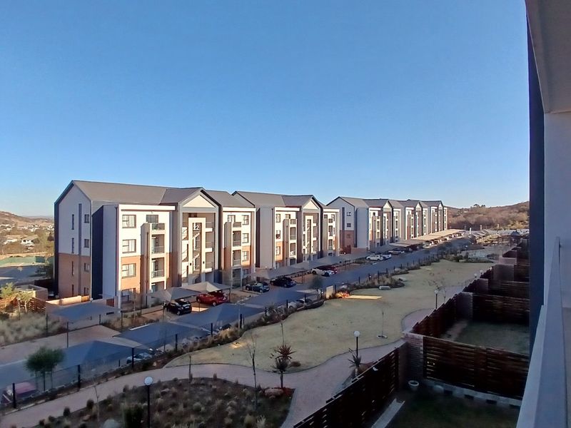 Elevated view overlooking a modern apartment complex with landscaped grounds, paved parking areas, and covered parking bays.