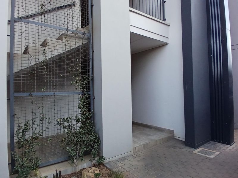 A modern apartment exterior featuring a paved walkway, concrete staircase enclosed by a metal mesh screen, and contemporary architectural finishes.