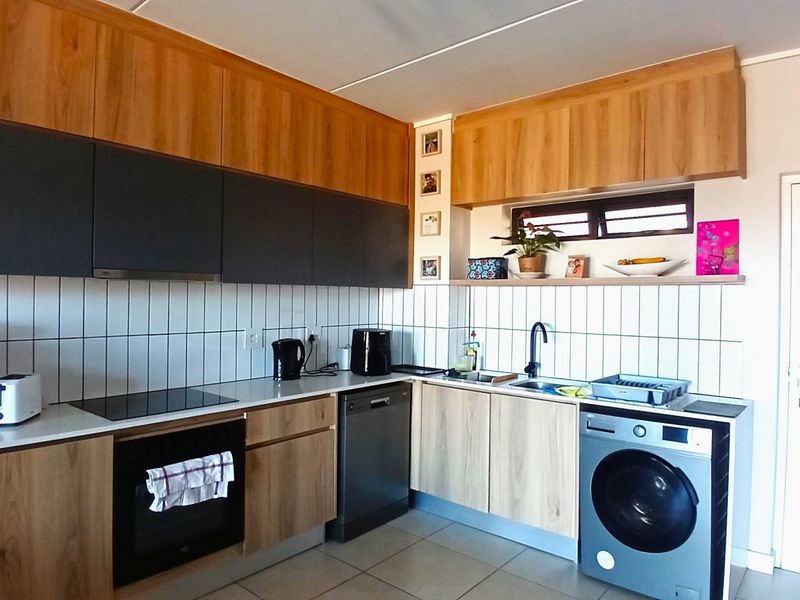 Modern kitchen featuring two-tone wood and dark grey cabinetry, tiled backsplash, built-in oven, electric hob, and integrated dishwasher.