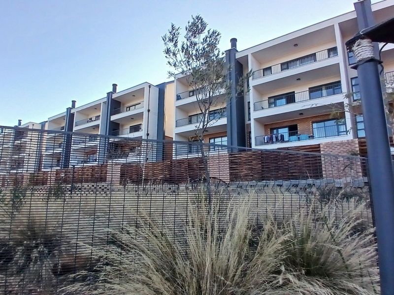 Exterior view of a modern apartment complex featuring multiple levels with private balconies, brick detailing, and secure perimeter fencing.