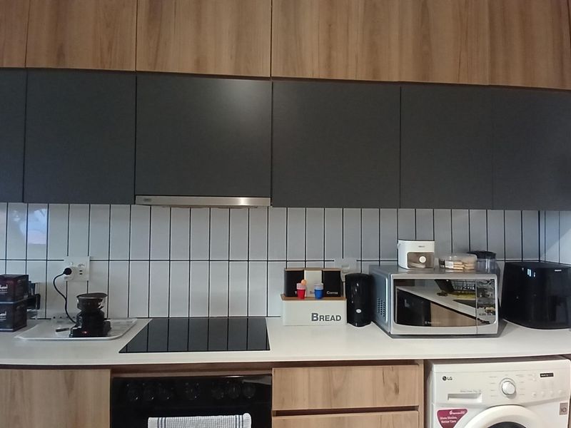Modern kitchen featuring wood-grain and matte grey cabinetry, white subway tile backsplash, integrated appliances, and a sleek electric hob.