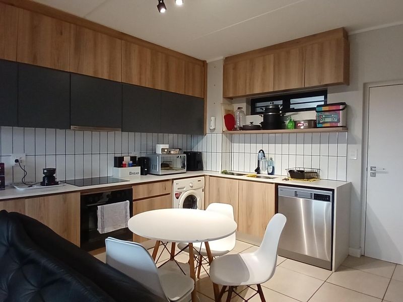 Modern open-plan kitchen featuring wood-finish cabinetry, integrated appliances, tiled backsplash, and neutral floor tiles, seamlessly connecting to the living area.