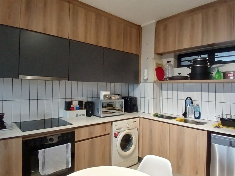 Modern kitchen featuring wood-tone and dark grey cabinetry, tiled backsplash, integrated appliances including a washing machine, dishwasher, and built-in oven with hob.