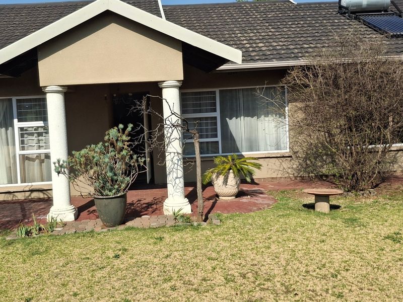 Rear view of the house featuring a covered patio with concrete columns, tiled roof with solar water heater, and paved outdoor area.