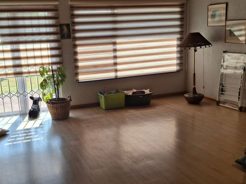 A living room featuring laminate flooring, large windows with roller blinds, and a sliding glass door providing access to the exterior.
