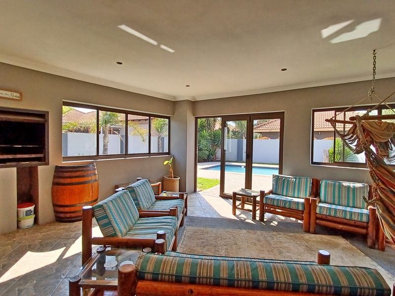 Spacious covered patio featuring a built-in braai, tiled flooring, and direct access to the pool area through sliding glass doors.