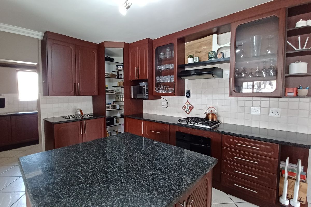 Spacious kitchen featuring dark wood cabinetry, granite countertops, a central island, built-in oven, gas hob, and a convenient walk-in pantry.