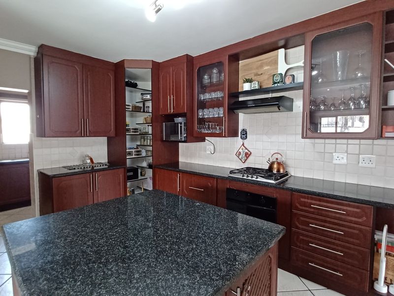 Spacious kitchen featuring dark wood cabinetry, granite countertops, a central island, built-in oven, gas hob, and a convenient walk-in pantry.