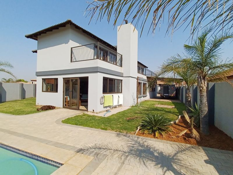 Rear view of a two-story house featuring a swimming pool, paved patio area, balcony, and a well-maintained garden with perimeter walling.