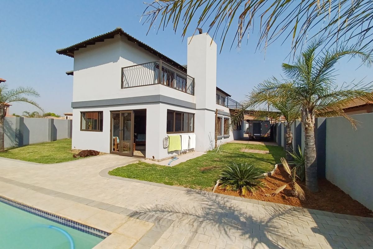 Rear view of a two-story house featuring a swimming pool, paved patio area, balcony, and a well-maintained garden with perimeter walling.
