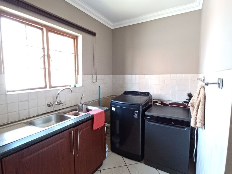 A functional laundry area featuring a stainless steel sink, granite countertops, tiled backsplash, and built-in cabinetry with space for appliances.
