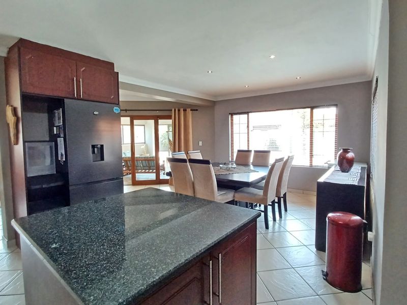 Open-plan kitchen and dining area featuring a granite-topped island, dark wood cabinetry, tiled flooring, and direct access to an adjoining living space.