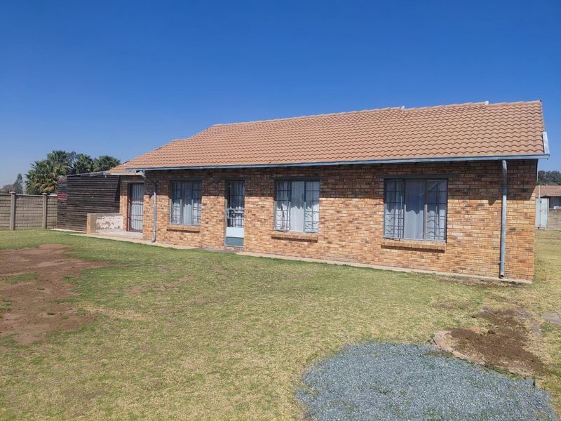 A rear view of a single-story face brick house featuring a tiled roof, security bars on windows, and a surrounding garden area.