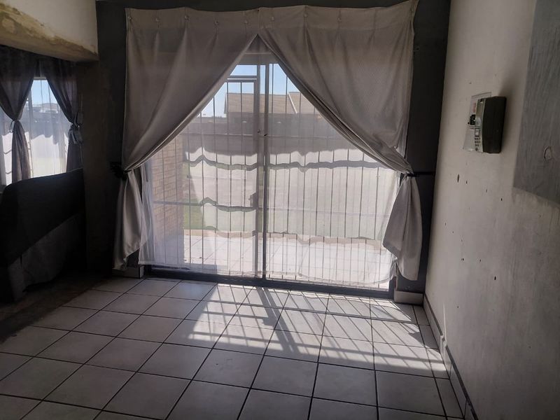 An empty living area featuring tiled flooring and a sliding glass door with security gate, providing access to the exterior.