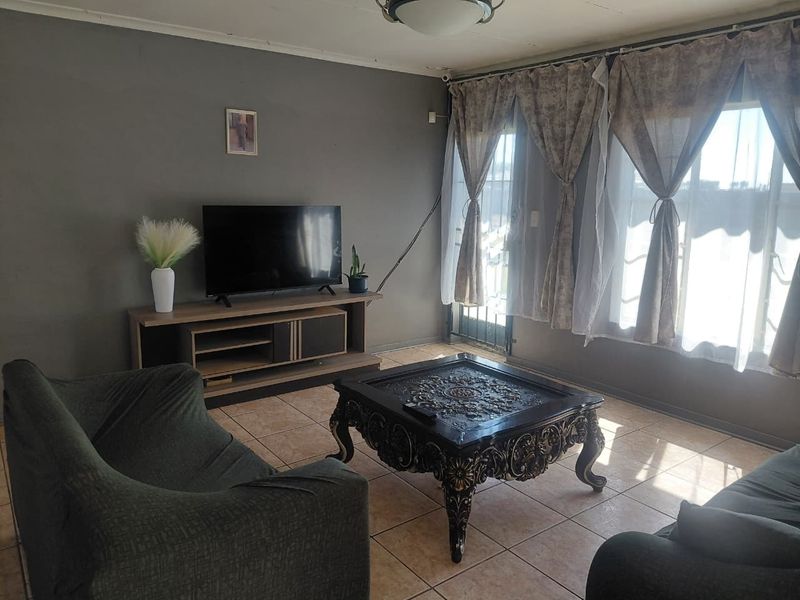 A living room featuring tiled flooring and a sliding glass door with security gate, providing access to the exterior.