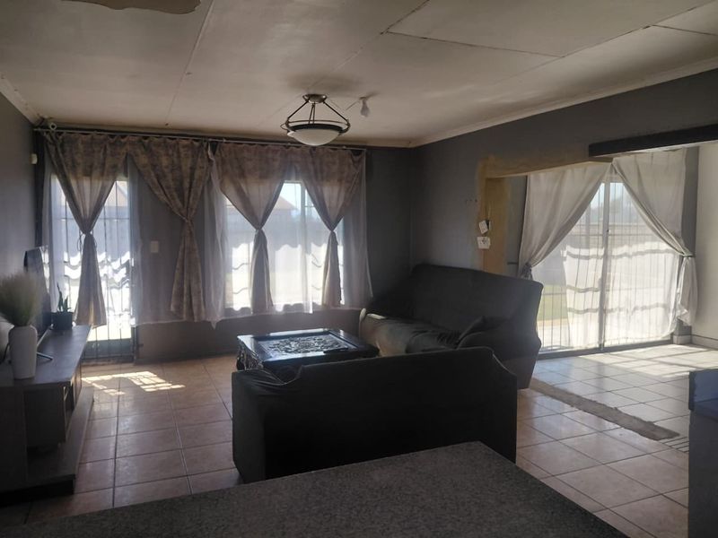 Spacious living area featuring tiled flooring and multiple sliding glass doors providing natural light, requiring some ceiling and wall finish repairs.