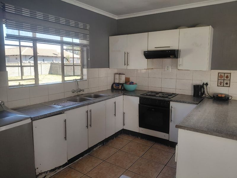 A functional kitchen featuring white cabinetry, a double basin sink, built-in oven with hob, extractor fan, and tiled flooring.