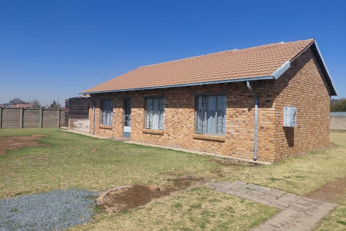 Rear view of a single-story face-brick house featuring a tiled roof, security bars on windows, and a surrounding garden with a precast boundary wall.