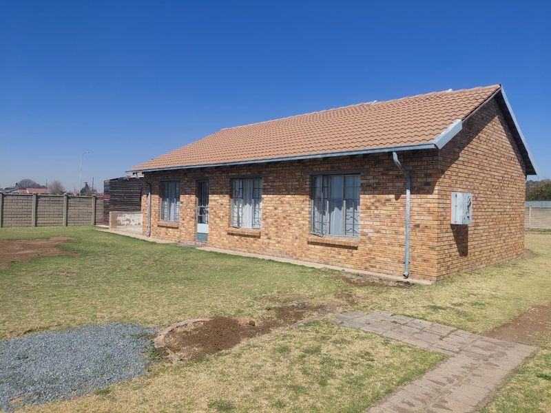 Rear view of a single-story face-brick house featuring a tiled roof, security bars on windows, and a surrounding garden with a precast boundary wall.
