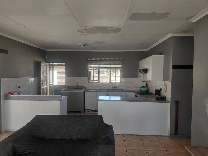 Open plan kitchen and living area featuring tiled floors, built-in cabinetry, and a breakfast counter, requiring ceiling repairs and cosmetic updates.