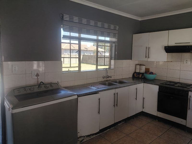 Functional kitchen featuring built-in cabinetry, double basin sink, integrated oven and hob, tiled backsplash, and tiled flooring.