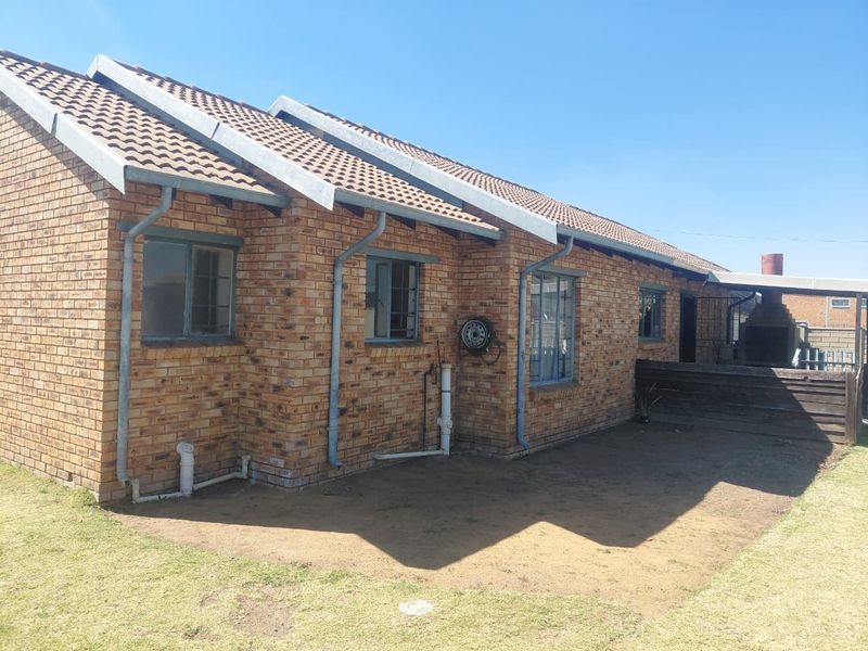 Rear view of the face brick house featuring a tiled roof, external plumbing, and a built-in braai area in the backyard.