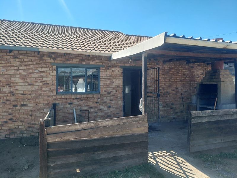 Rear exterior view featuring a brick facade, covered patio area with a built-in braai, and timber fencing.