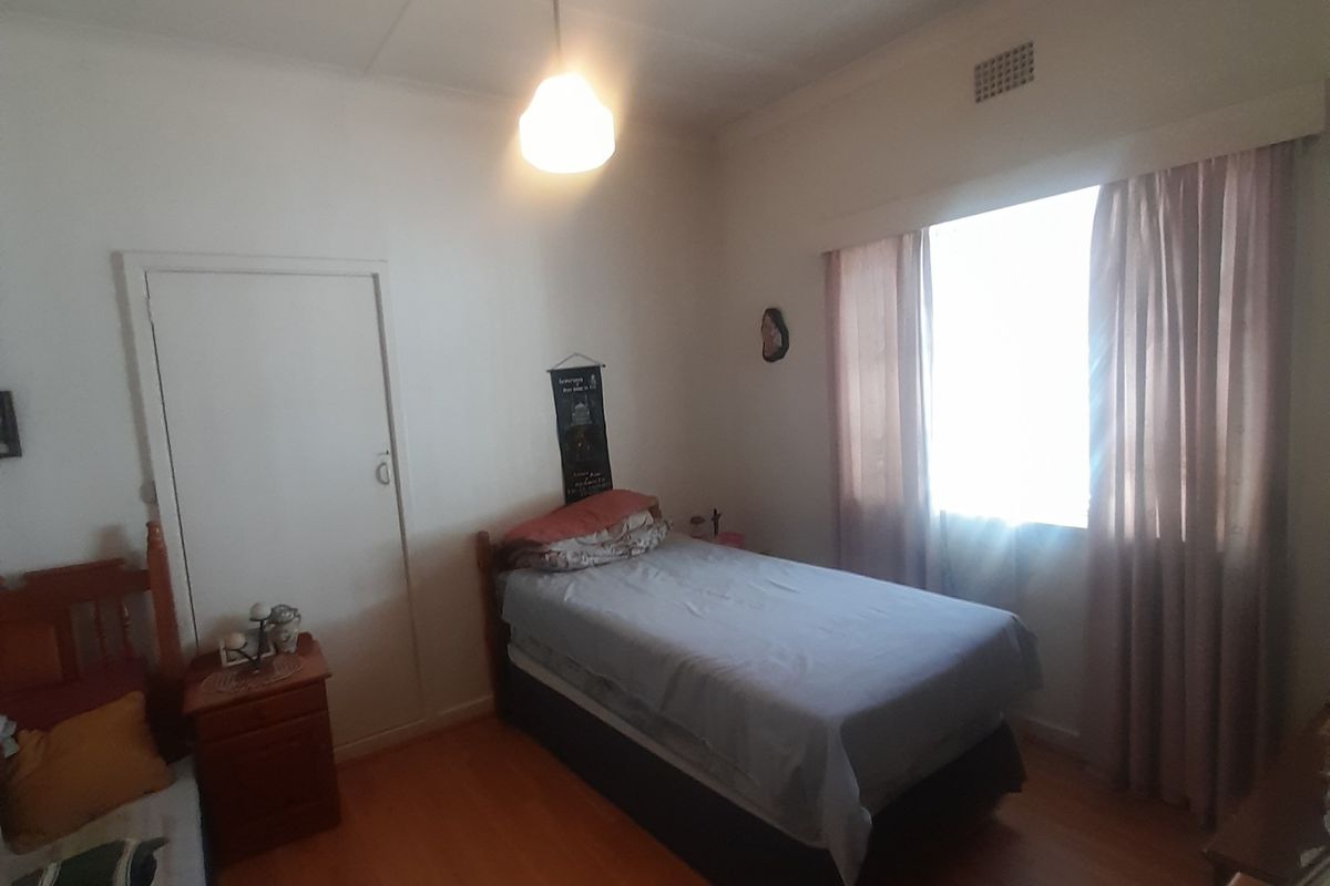 A standard bedroom featuring laminate flooring, a central ceiling light, and a window with curtains, providing a functional and neutral living space.