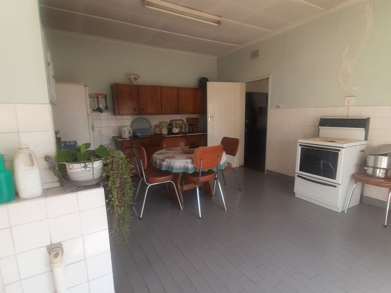 A dated kitchen featuring tiled flooring, wall tiling, and built-in wooden cabinetry, requiring cosmetic updates and repairs to the wall finish.