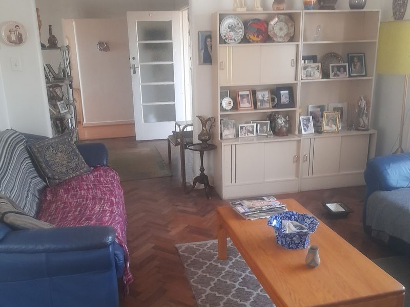 A living room featuring classic herringbone parquet flooring and a built-in shelving unit, leading through to an internal hallway.