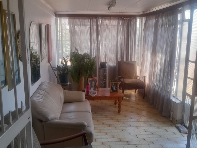A sunlit living area featuring tiled flooring and large windows, providing a bright and comfortable space for relaxation.