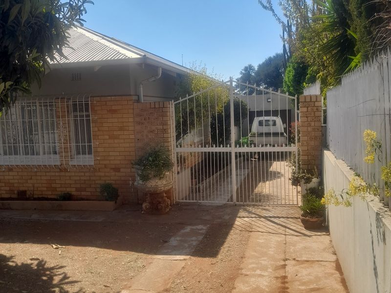 Front exterior view of a brick house featuring a gated driveway, security bars on windows, and a corrugated metal roof.