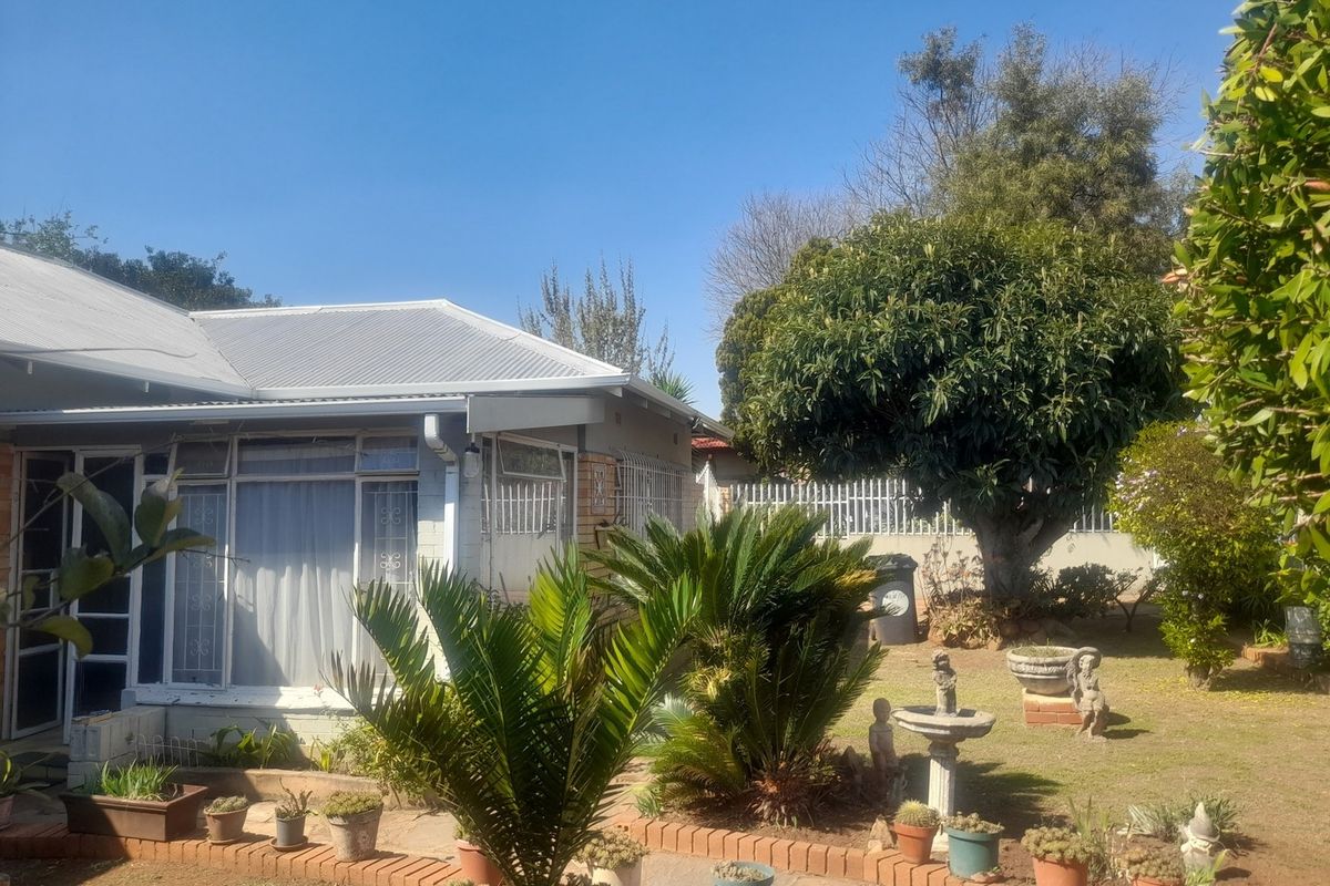 A view of the rear garden featuring a paved walkway, brick edging, and established landscaping adjacent to the house with a metal roof.