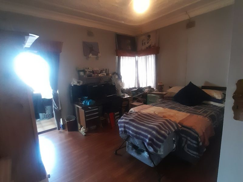 A bedroom featuring laminate flooring, a decorative ceiling rose, and a central ceiling fan, offering a functional space with potential for cosmetic updates.