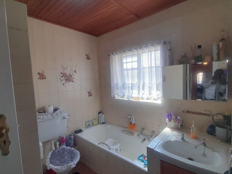 A dated bathroom featuring a built-in bathtub, vanity cabinet with basin, and wall-mounted toilet, finished with timber ceiling and ceramic wall tiles.